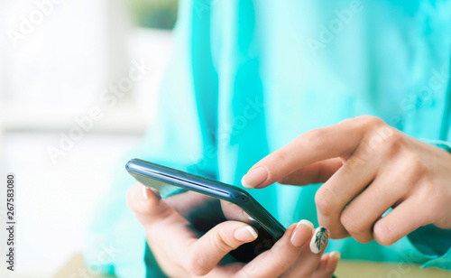 Young woman using smartphone for surfing and browsing Internet  searching for required information  sitting at desk with laptop.