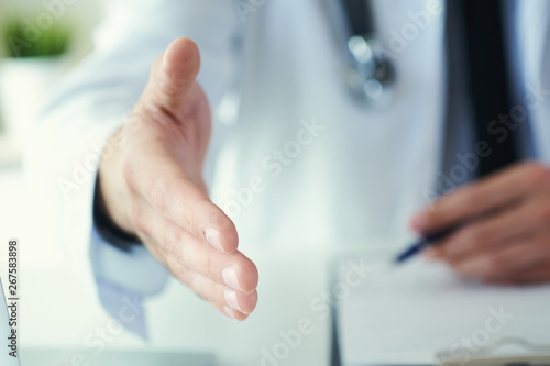 Male medicine doctor offering hand to shake in office closeup. Greeting and welcoming gesture. Medical cure and tests advertisement concept.
