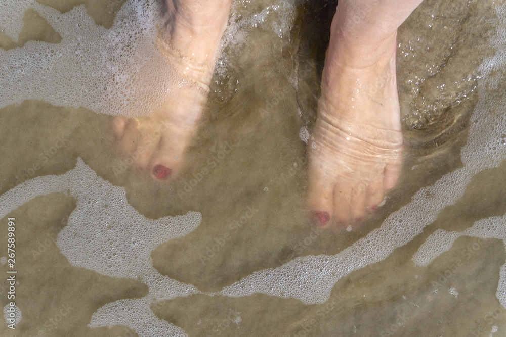 Fototapeta premium Naked feet with red nail polish in the sand on the beach