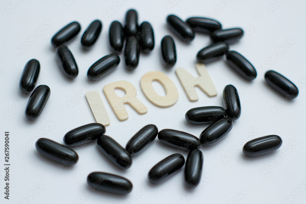 Iron medicament supplement. Black capsules with liquid inside. Inscription Iron by wooden letters. Iron medicament supplement. Black capsules with liquid inside. Inscription Iron by wooden letters.
