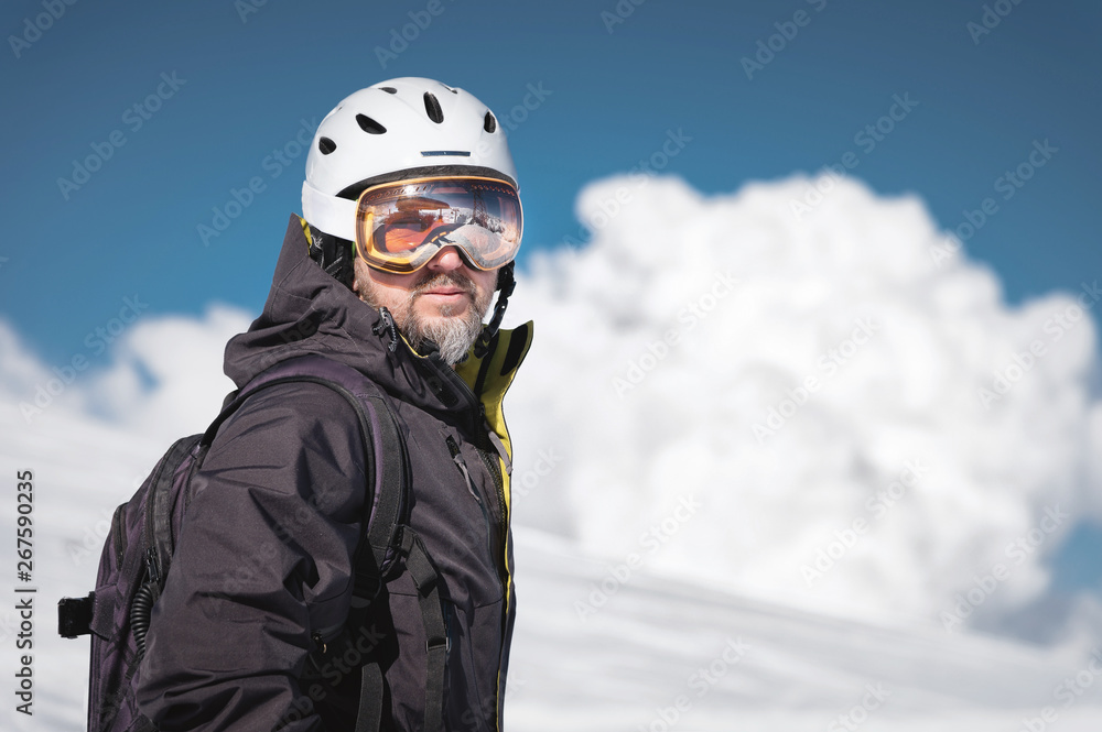 Close-up athlete skier in helmet and ski mask against the snow-capped mountains of a ski resort with a reflection of the Caucasian mountains in the mask