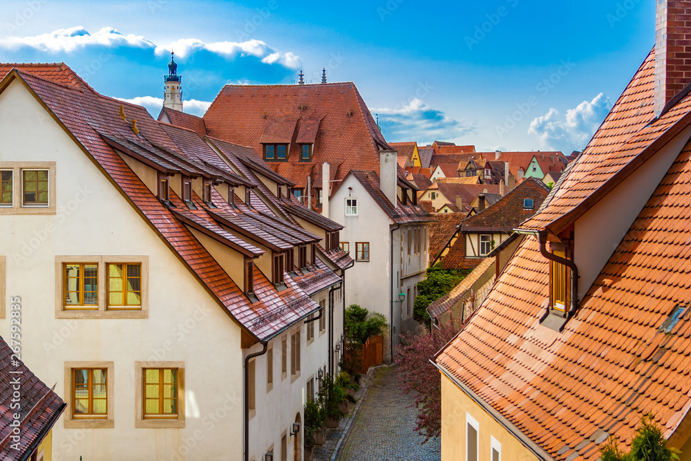 Picturesque rooftop view of a typical lane in the medieval town Rothenburg ob der Tauber with colourful timber framed houses, a blue sky and the tip of the historic clock tower of the town hall.