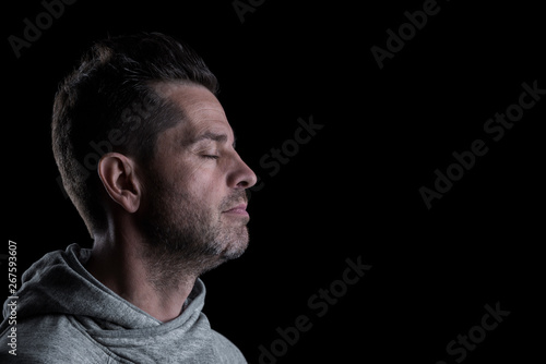 Side studio portrait of a serious man with closed eyes. Isolated on black background. Horizontal. Copyspace.