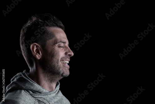 Side studio portrait of a smiling man with closed eyes. Isolated on black background. Horizontal. Copyspace.