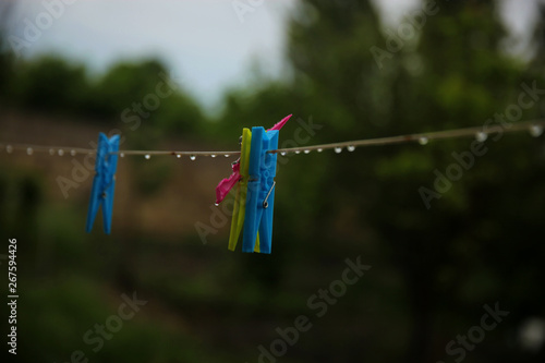 Wet colorful pegs hanging on a clothesline after the rain in the backyard. No clothes outside, it’s time to use dryer.