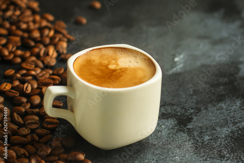 coffee in a white cup and coffee grain scattered on the table (freshly brewed hot drink with foam). food background. top