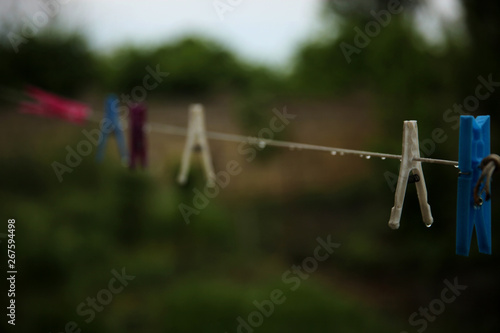 Wet colorful pegs hanging on a clothesline after the rain in the backyard. No clothes outside, it’s time to use dryer.