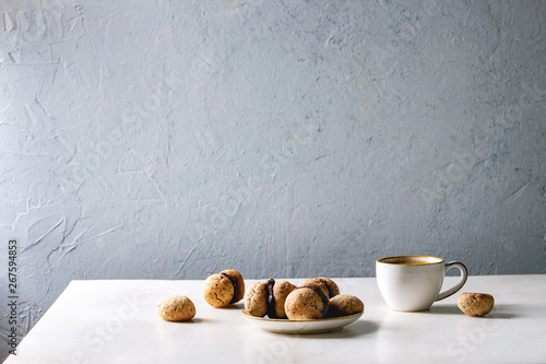 Baci di dama homemade italian hazelnut biscuits cookies with chocolate cream served in ceramic plate with cup of espresso coffee over white marble table. Copy space