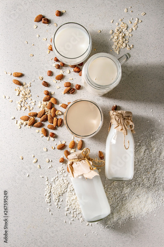 Fotografija Variety of non-dairy vegan lactose free nuts and grain milk almond, hazelnut, coconut, rice, oat in glass bottles with ingredients above over white spotted background