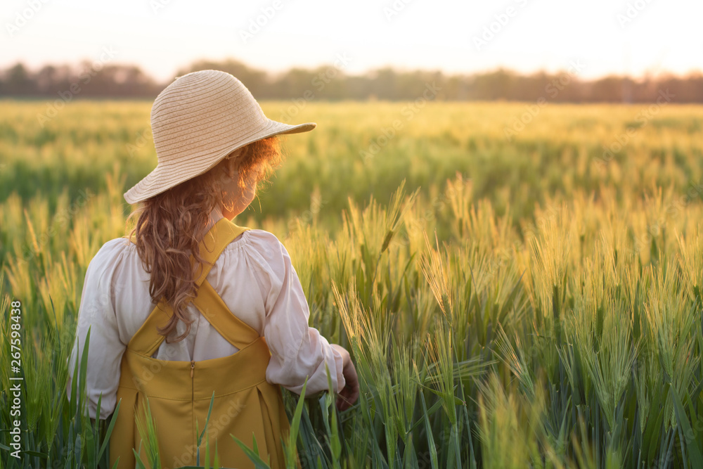 Obraz premium The child is a blonde curly-haired girl in a straw hat in a wheat field at sunset. Beautiful, romantic scene. The concept of organic farming and healthy lifestyle, healthy food. The concept of dreams,