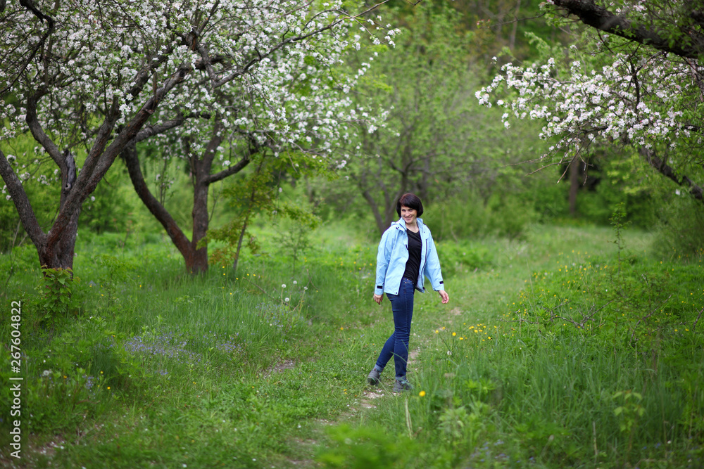 Beautiful mature woman posing for the camera in the spring garden. The girl enjoys the flowering of apple trees. Beautiful mature woman posing for the camera in the spring garden. The girl enjoys the flowering of apple trees.