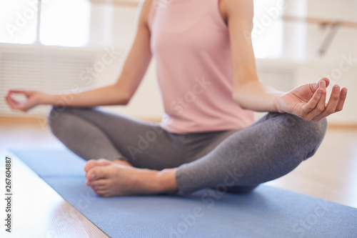 Close-up of unrecognizable woman in gray leggings sitting in butterfly pose and keeping hands in mudra while keeping calm at yoga