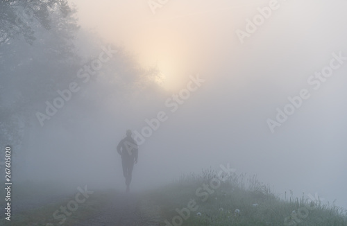Athlete running on a gravel road during a foggy, spring sunrise in the countryside. © sanderstock