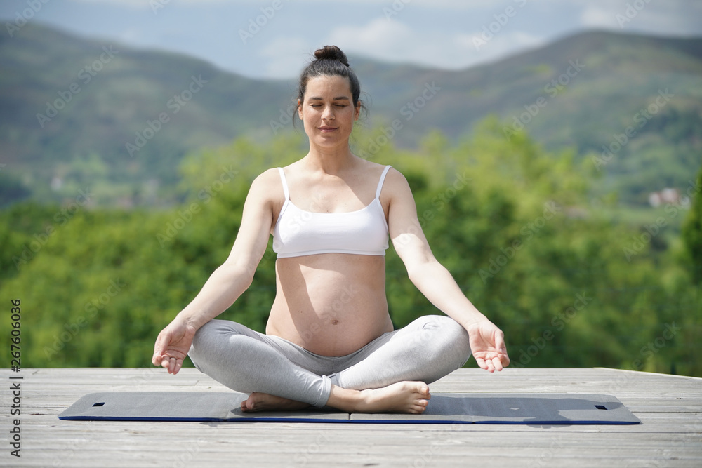 Pregnant woman doing yoga exercises outside