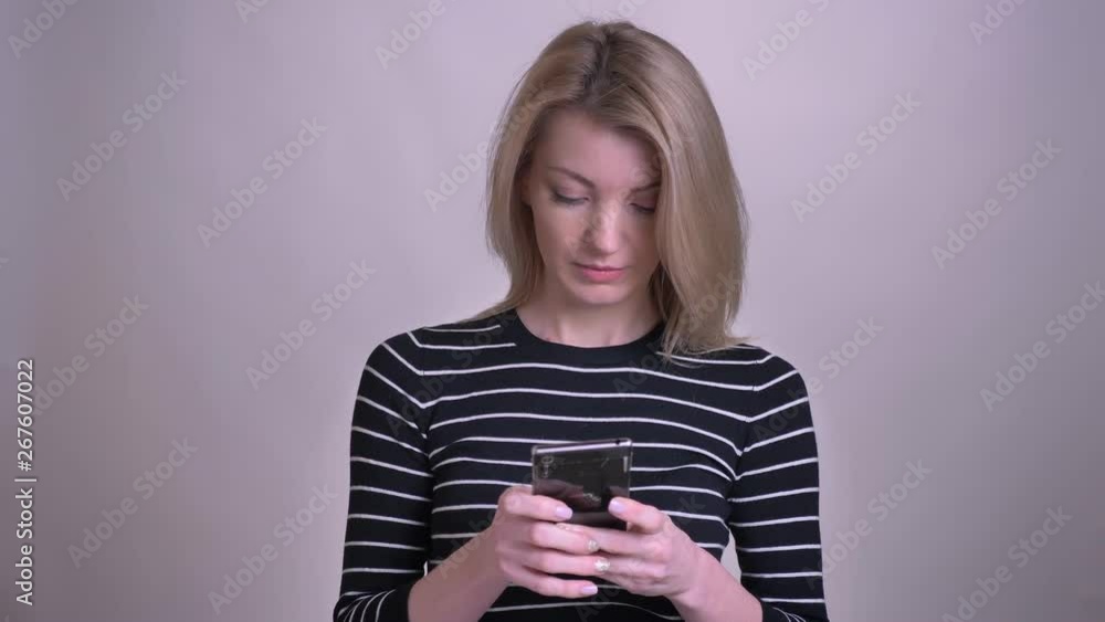 Closeup portrait of adult attractive blonde caucasian female texting on the phone and smiling with background isolated on white Closeup portrait of adult attractive blonde caucasian female texting on the phone and smiling with background isolated on white