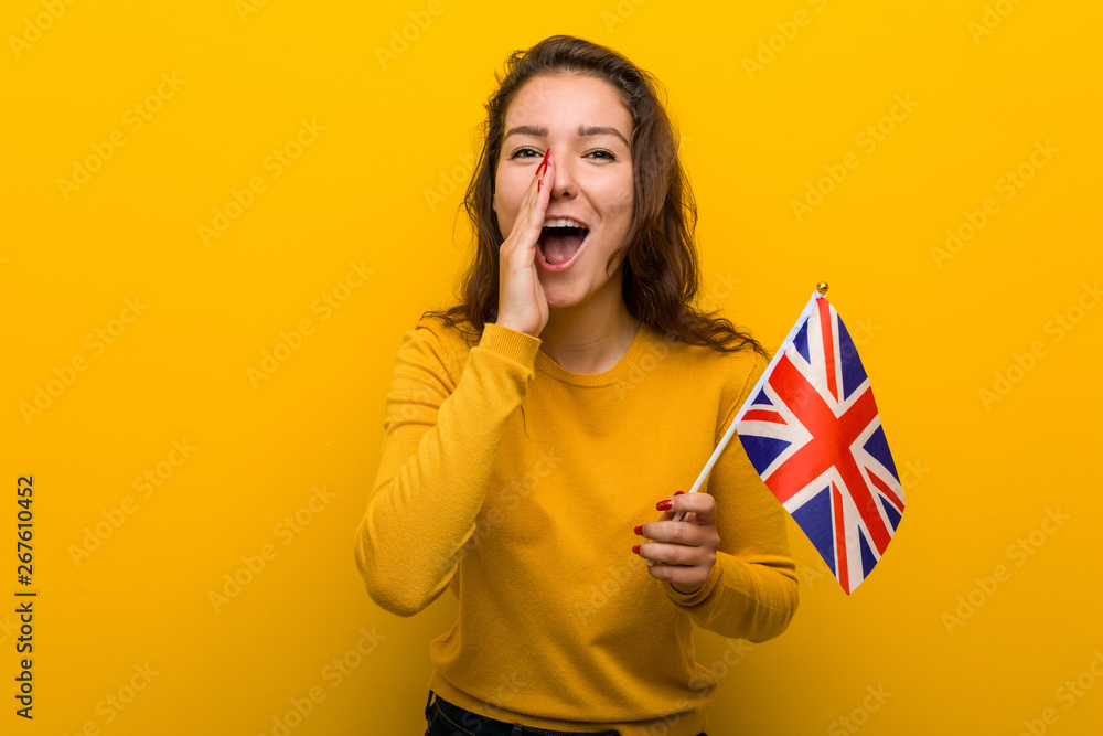 © Asier - Young european woman holding an united kingdom flag shouting excited to front.