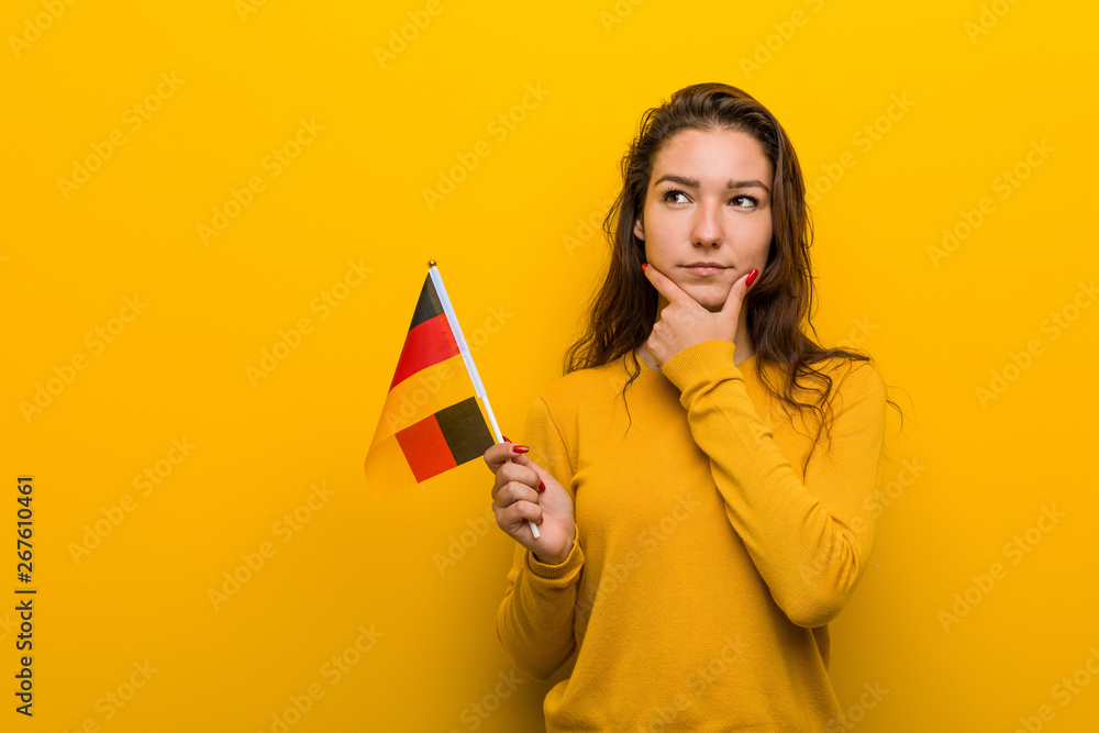 Young european woman holding a germany flag looking sideways with doubtful and skeptical expression.