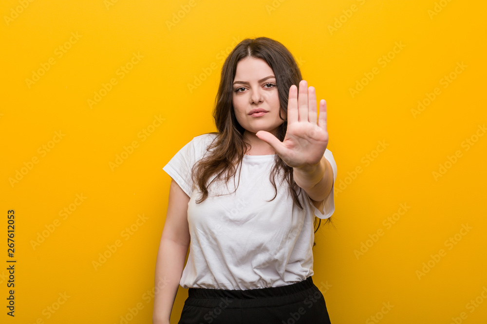 Young curvy plus size woman standing with outstretched hand showing stop sign, preventing you. Young curvy plus size woman standing with outstretched hand showing stop sign, preventing you.