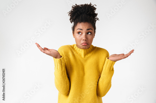 Fototapeta Beautiful young african confused woman posing isolated over white wall background