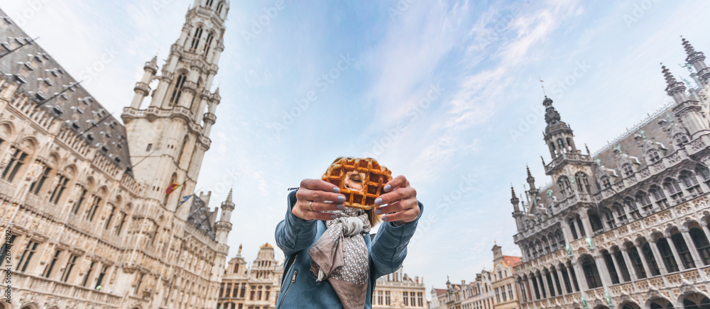 Fototapeta premium Young beautiful woman holding a traditional Belgian waffle on the background of the Great Market Square in Brussels, Belgium