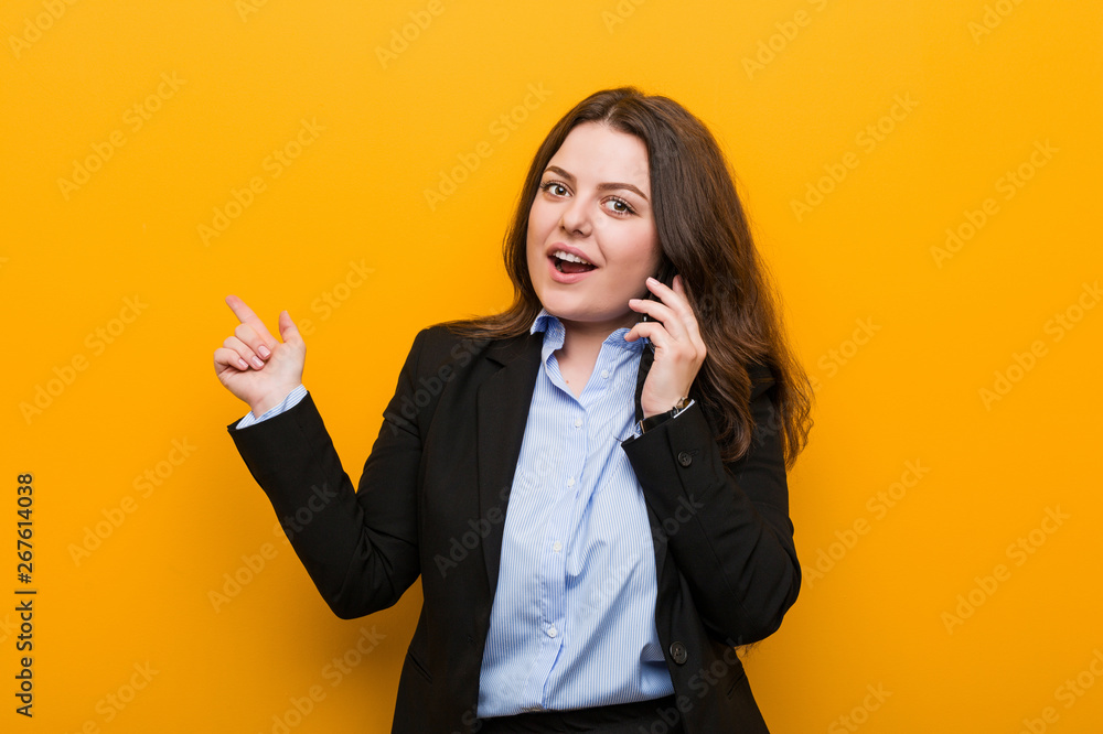 Young curvy plus size business woman holding a phone smiling cheerfully pointing with forefinger away. Young curvy plus size business woman holding a phone smiling cheerfully pointing with forefinger away.