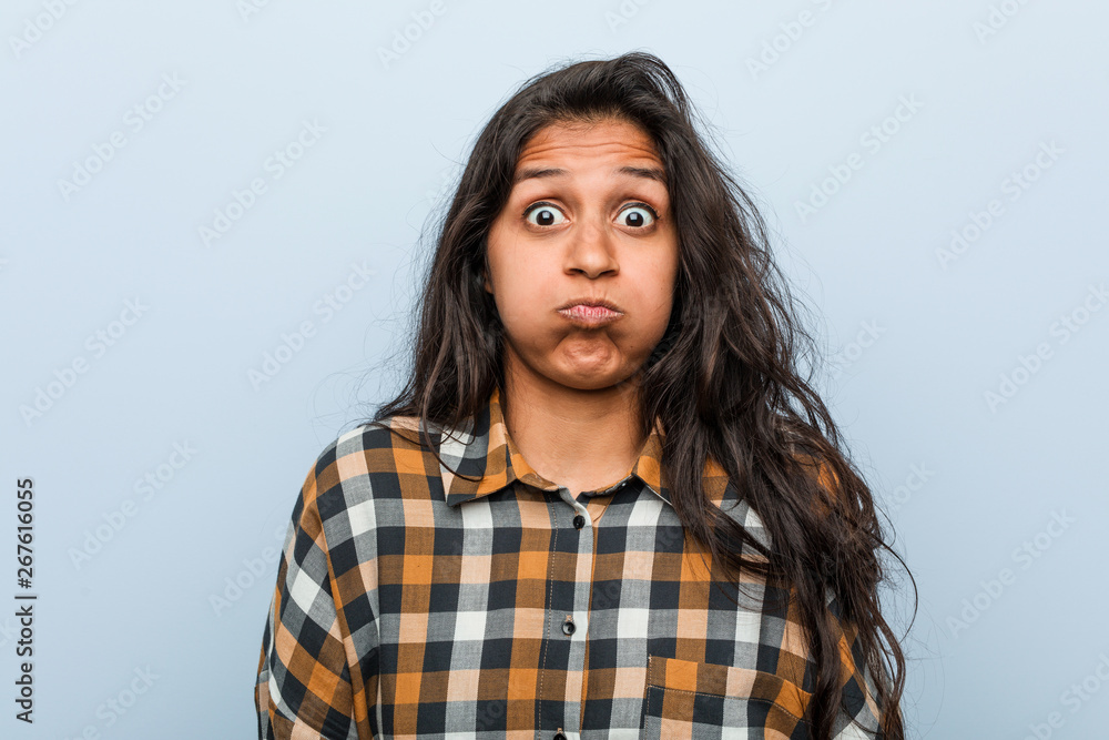 Young cool indian woman blows cheeks, has tired expression. Facial expression concept. Young cool indian woman blows cheeks, has tired expression. Facial expression concept.