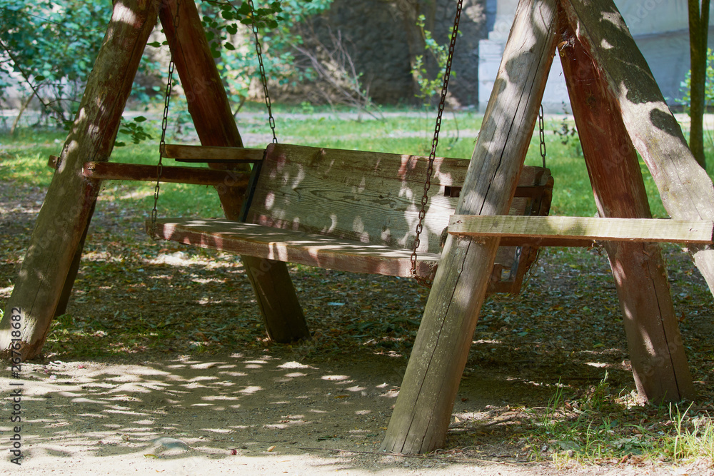 Fototapeta premium Old wooden swing on an iron chain in park.