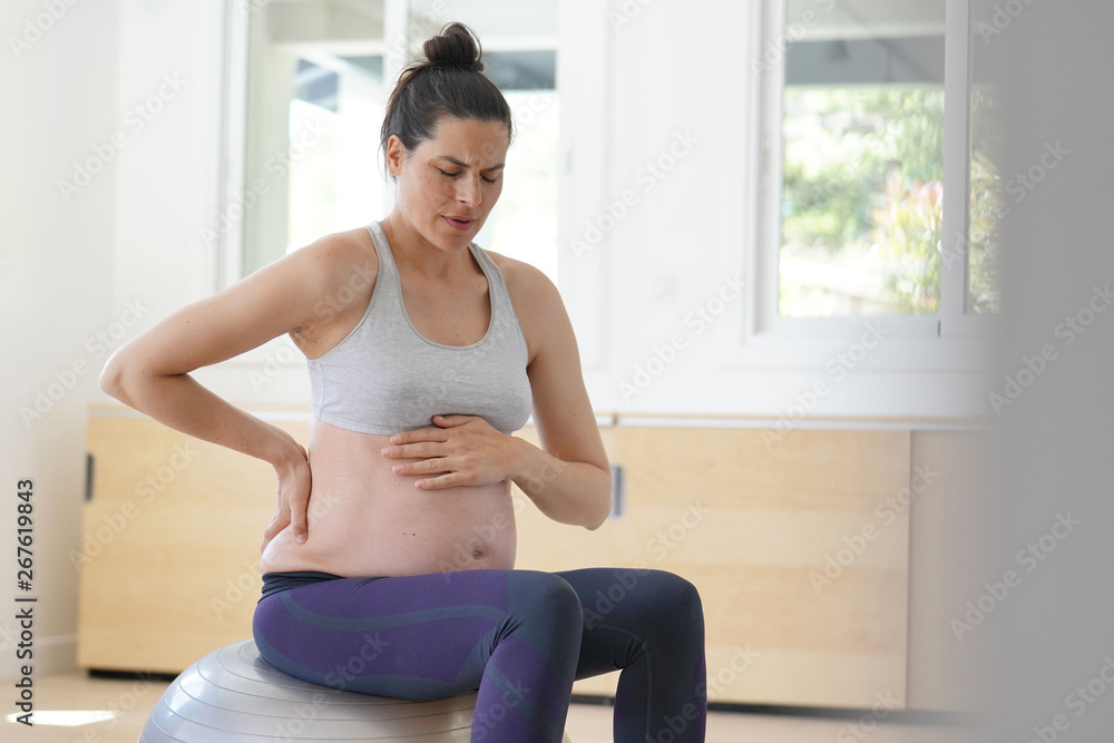 Pregnant woman at home sitting on fitness ball, doing relaxation exercises Pregnant woman at home sitting on fitness ball, doing relaxation exercises