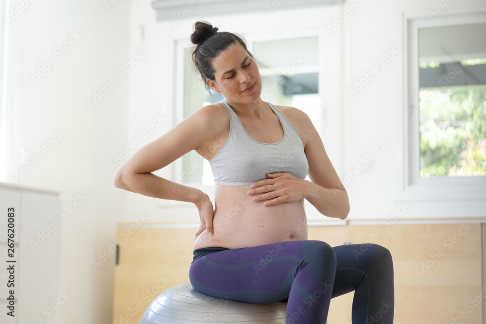 Pregnant woman at home sitting on fitness ball, doing relaxation exercises