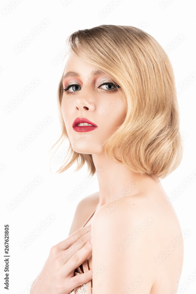Cute blond girl with big beautiful eyes, red lips and vintage style hairstyle, wearing a golden sparkling dress touches her chest. Isolated on white background. Clean, healthy skin. Cute blond girl with big beautiful eyes, red lips and vintage style hairstyle, wearing a golden sparkling dress touches her chest. Isolated on white background. Clean, healthy skin.