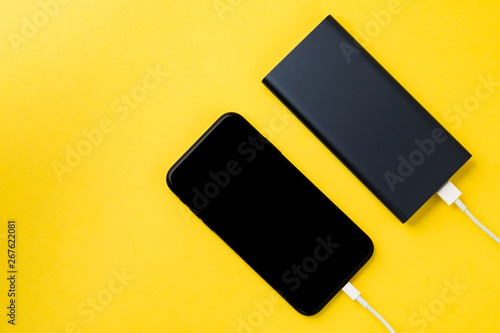 Smartphone charging with power Bank via USB cable on yellow background top view.