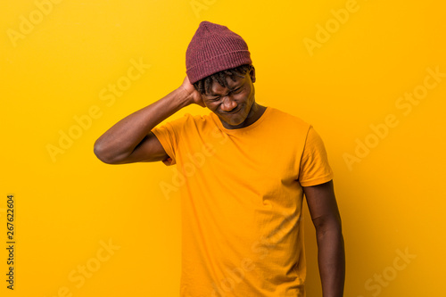 Young black man wearing rastas over yellow background suffering neck pain due to sedentary lifestyle. © Asier