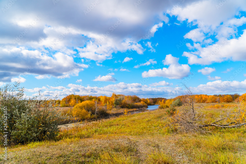 Blue sky with clouds, small river, orange leaves on trees