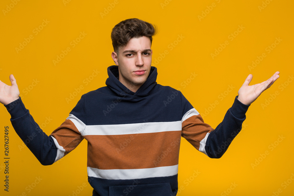 Fototapeta premium Young cool man wearing a hoodie doubting and shrugging him shoulders in questioning gesture.