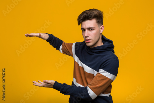 Young cool man wearing a hoodie shocked and amazed holding a copy space between hands.