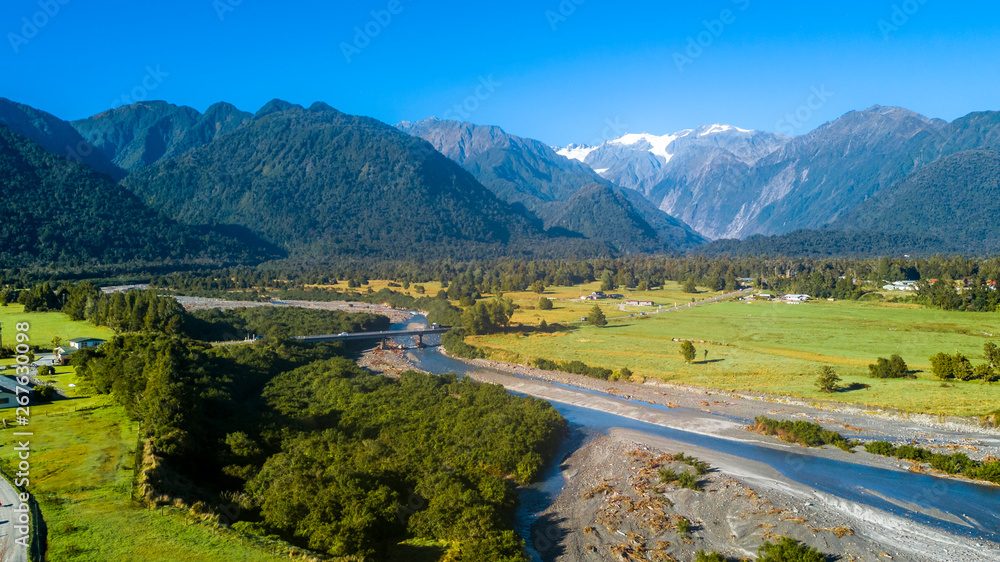 River running through sunny valley with high mountains on the background. West Coast, South Island, New Zealand