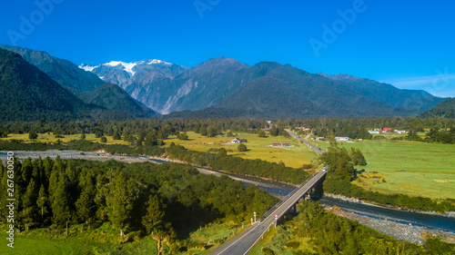 Bridge across the river in the middle of sunny valley with snowy mountains on the background. West Coast, South Island, New Zealand