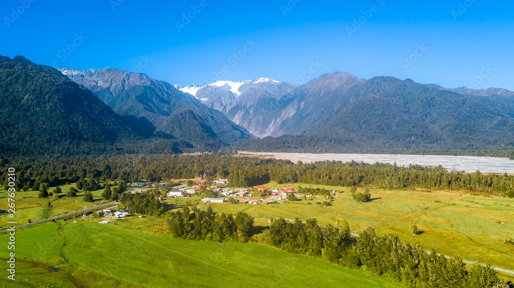 Small village in the middle of sunny valley with snowy mountains on the background. West Coast, South Island, New Zealand
