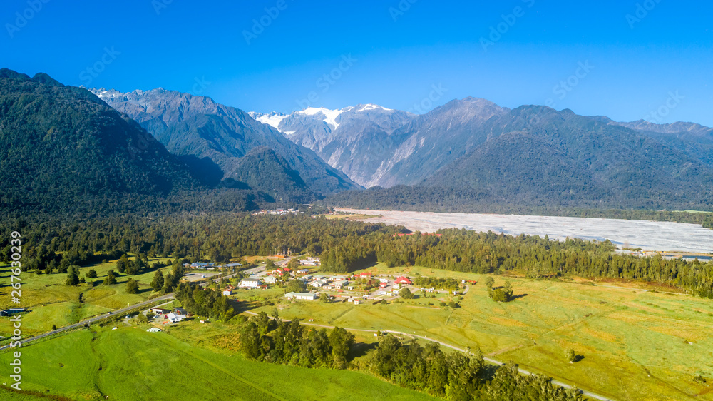 Small village in the middle of sunny valley with snowy mountains on the background. West Coast, South Island, New Zealand