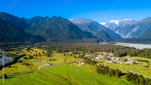Small village in the middle of sunny valley with snowy mountains on the background. West Coast  South Island  New Zealand