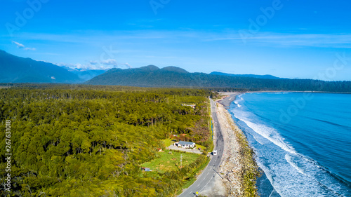 Road running along a sunny beach with a peninsula and mountains on the background. West Coast  South Island  New Zealand