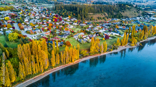 Photos Yellow autumn trees on the sore of pristine lake with small town on the background