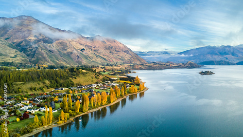 Canvastavla Small town surrounded by yellow autumn trees on a shore of pristine lake with mountains on the background