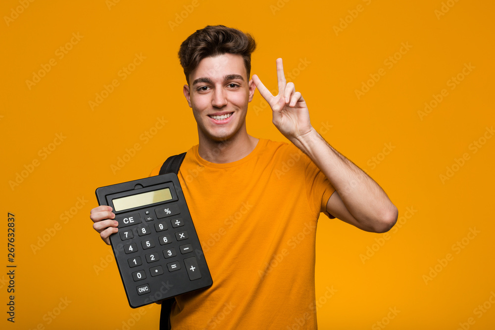 Young student man holding a calculator looking sideways with doubtful and skeptical expression. - obrazy, fototapety, plakaty 