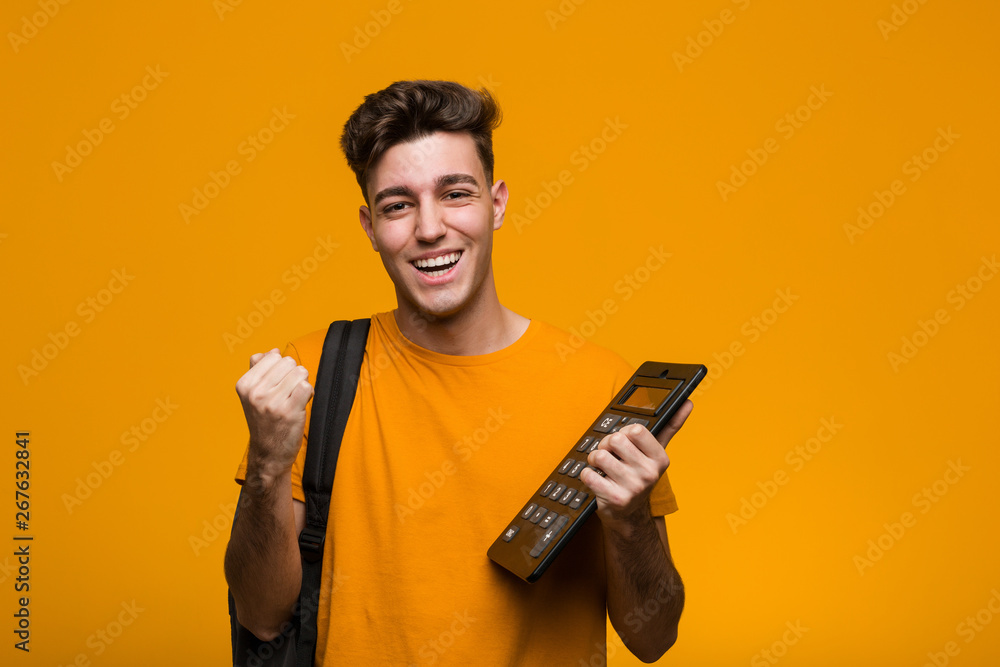Young student man holding a calculator celebrating a victory or success - obrazy, fototapety, plakaty 