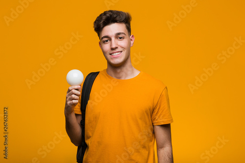 Young student man holding a light bulb smiling and raising thumb up