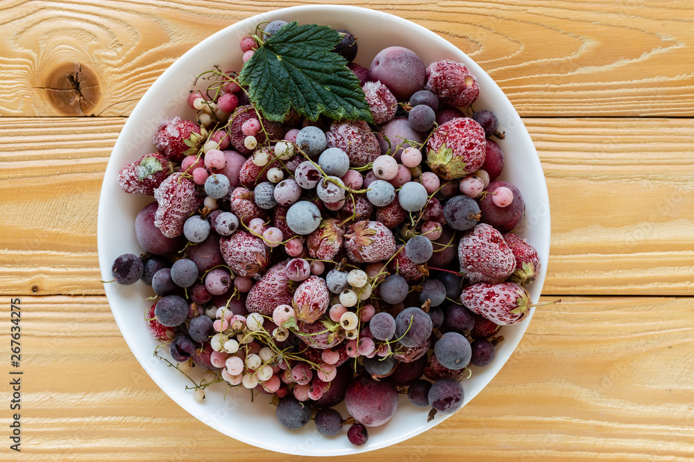frozen berries, black currant, red currant, raspberry, blueberry in bowl decorated by currant leaf on wooden table in rustic style, top view. frozen berries, black currant, red currant, raspberry, blueberry in bowl decorated by currant leaf on wooden table in rustic style, top view.
