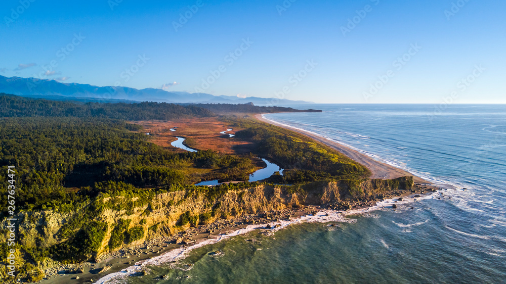 Sunset over remote beach on the coast on Tasman sea with native forest and mountains on the background. West Coast, South Island, New Zealand