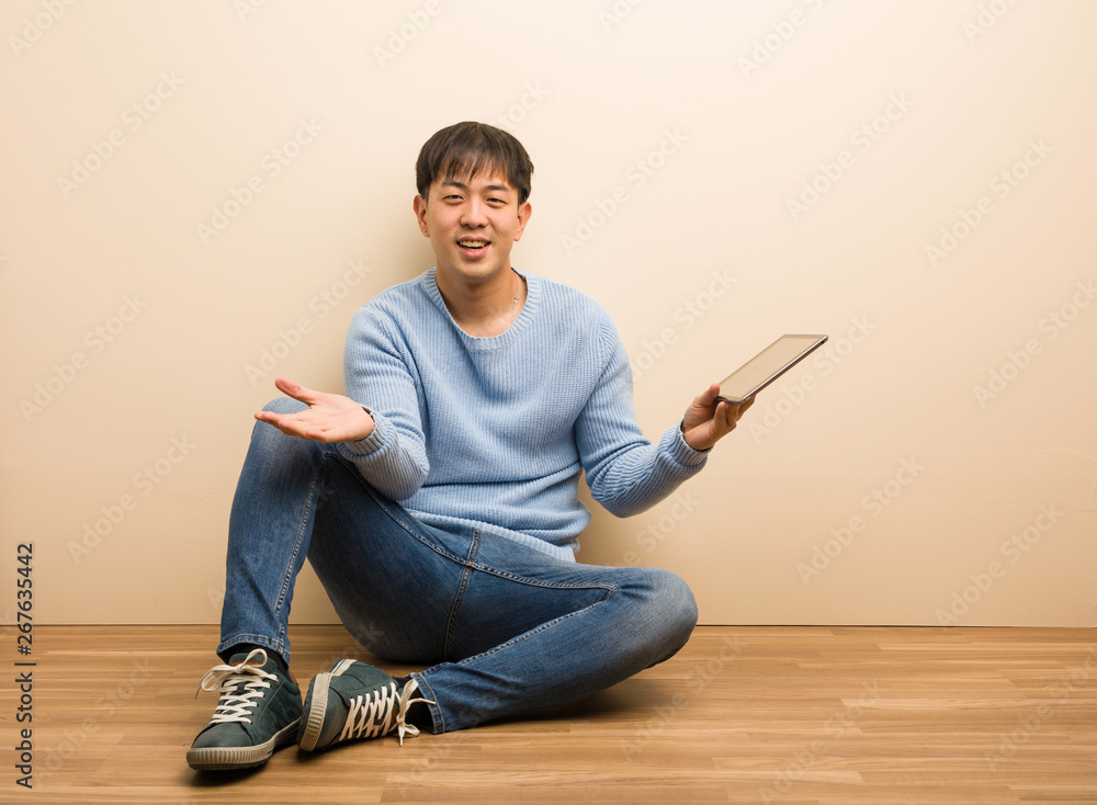 Young chinese man sitting using his tablet inviting to come Young chinese man sitting using his tablet inviting to come