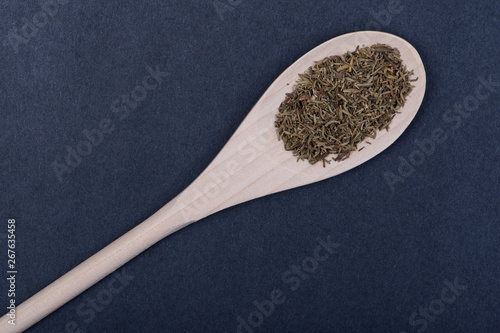 Heap of Dried Organic Culinary Thyme Herb in handmade wooden spoon on dark background. Thymus vulgaris.